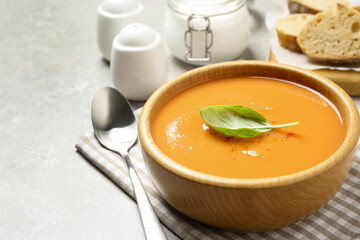 Tasty creamy pumpkin soup with basil in bowl on grey table