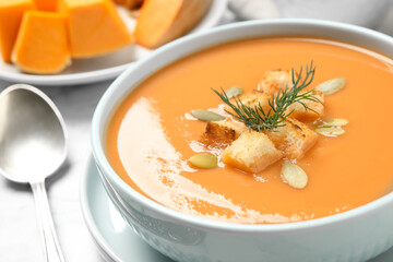 Tasty creamy pumpkin soup with croutons, seeds and dill in bowl on table, closeup