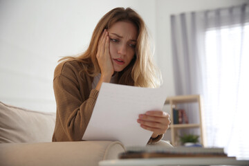 Worried woman reading letter on sofa at home
