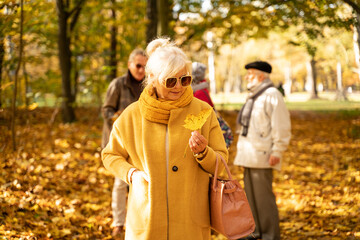 Senior woman with friends on the walk in autumn beautiful park.