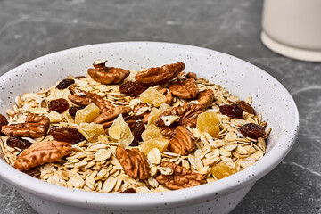 Muesli or granola with dried fruits and pecans nuts in white bowl on gray stone table. Healthy breakfast. Kinfolk style.