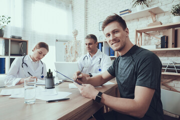 A male athlete sits at doctor office and signs.