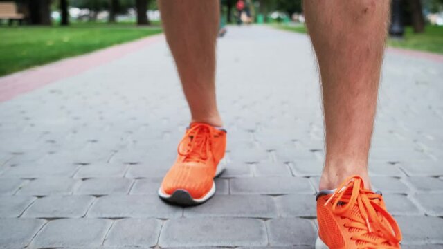Man in orange trainers stepping along paved alley in city park