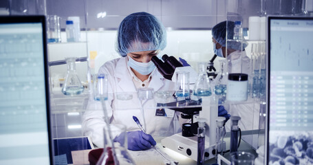 Female science team working on biohazardous samples. Using microscope and computer with data