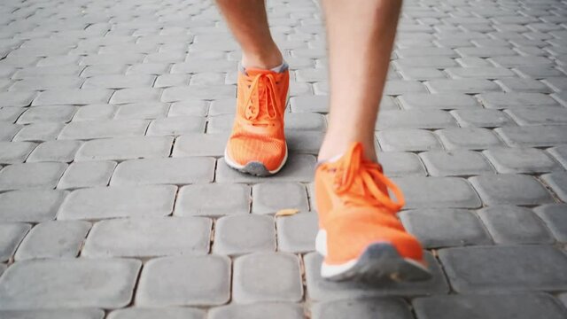 Man in orange trainers stepping along paved alley in city park