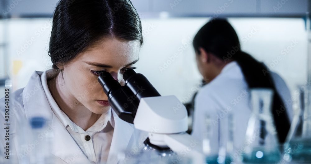 Wall mural multi ethnic science team working with microscope and computer. female doctors in futuristic laborat