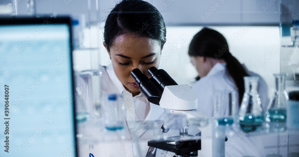 Wall mural multi ethnic science team working with microscope and computer. female doctors in futuristic laborat