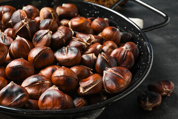 Delicious roasted edible chestnuts in frying pan on black table, closeup