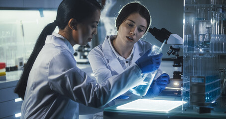 Multi ethnic female scientists working late in labolatory. Using microscope