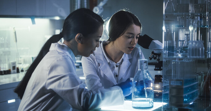 Multi Ethnic Female Scientists Working Late In Labolatory. Using Microscope