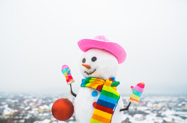 Snowwoman with Christmas toy. Snowman holds new year ball. Snow man in pink hat. Christmas. Funny snowman in stylish hat and scarf. Merry Christmas and Happy new year.