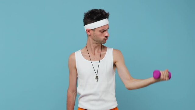 Strong young fitness man with thin skinny body sportsman in white headband shirt isolated on blue background. Workout gym sport motivation concept. Doing exercise point on dumbbells showing thumb up