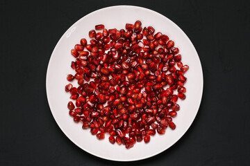 Pomegranate seeds on a plate isolated on a black background. Peeled fresh pomegranate. Healthy healthy food with vitamins
