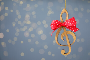 Wooden music note with red bow hanging on light blue background with Christmas lights. Space for...