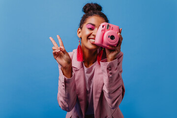 Positive girl in pink earrings taking pictures. Lovely african woman holding camera on blue...