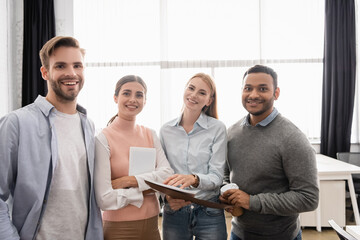 Multiethnic businesspeople with paper folder and digital tablet smiling at camera in office