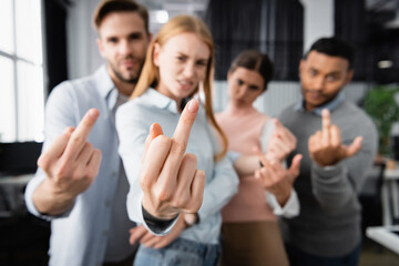 Multicultural businesspeople on blurred background showing middle fingers in office