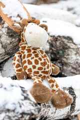 Children's toy giraffe in the snow on birch logs outside a winter country cottage