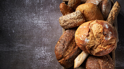 Banner with different Types of Bread put in a wooden box on dark background. Bakery concept. Close up. Empty space for text.