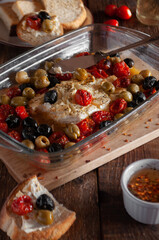 Baked feta cheese with cherry tomatoes, olives, olives, herbs and olive oil, in a glass form, on a wooden background