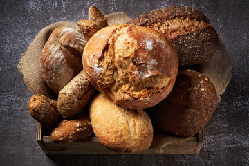 Different Types of Bread put in a wooden box on dark background. Bakery concept. Close up.