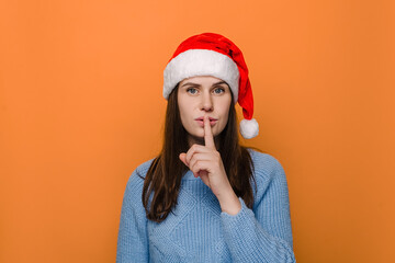 Beautiful young female holding finger at her lips asking not to make noise or hold tongue and...