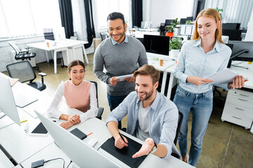 Obraz premium Smiling multicultural businesspeople using graphics tablet and computer in office