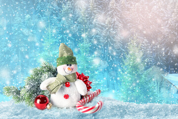 Cute toy snowman with candy cane, fir tree branch and Christmas ball on blurred background. Space...