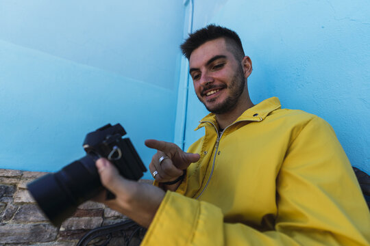 Cheerful male with a nose piercing wearing a yellow jacket and looking at the pictures in a camera