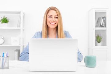 A young woman sits at a table and uses a laptop. Freelance or office work.