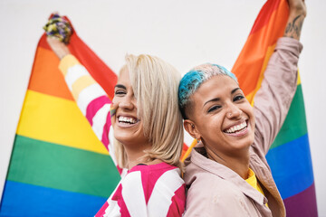 Cheerful young couple of women with lgbt rainbow flag at gay pride event - Focus on faces