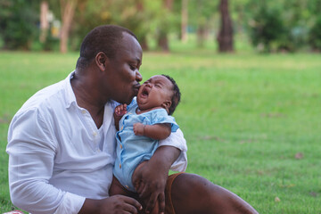 Moment of happiness between dark skinned father and daughter, father comforting the crying newborn baby and hold her in his arms, at park