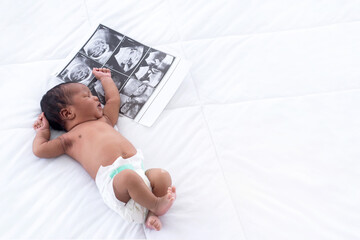 Newborn baby with ultra sound scan photo on bed, top view