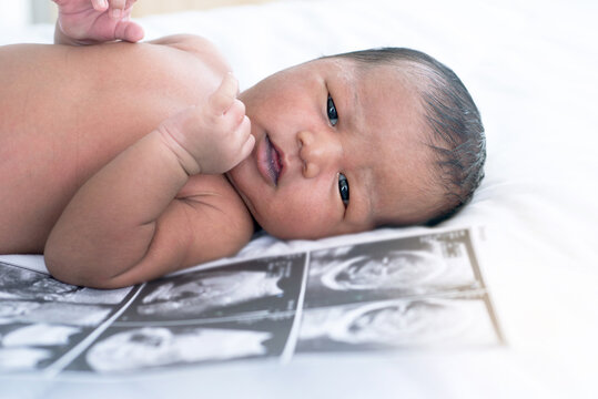Close up, newborn baby with ultra sound scan photo on bed, looking at camera
