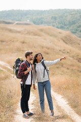 African american woman pointing with finger near smiling boyfriend with backpack on path outdoors