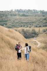 Interracial couple with backpacks holding hands on grassy hill during trip