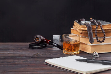 Still life vintage writers accessories. Notepad with pen with glass of cognac, smoking pipe, stack of books and watch clock on wooden table.