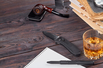 Short knife with smoking pipe and glass of cognac. Top view notepad and stack of books.