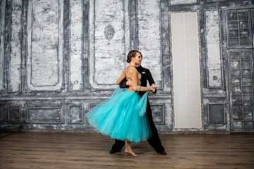 a young man in a black suit is dancing with a girl in a turquoise dress in the dance hall