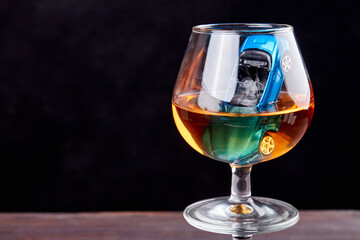 Composition with miniature car in a glass of whiskey. Drive drunk concept. Isolated on black background.