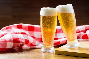 Two glasses of beer against a plaid towel on wooden table