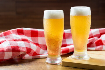 Two glasses of beer against a plaid towel on wooden table