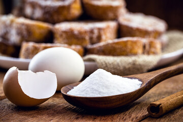 wooden spoon with refined sugar and eggs on the side, rustic kitchen concept. Spot focus, toast in the background