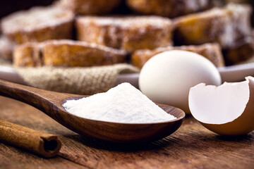 wooden spoon with refined sugar and eggs on the side, rustic kitchen concept. Spot focus, toast in the background