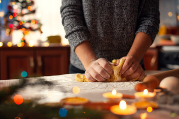 Close-up picture of hands of a girl making dough on the table decorated with christmas candles,...