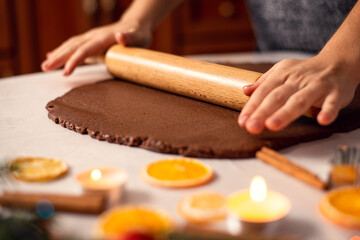 Fototapeta na wymiar Close-up shot of a rolling pin in hands of a girl rolling dark chocolate dough. Christmas preparations