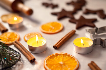 Burning candles, cinnamon, dried orange, raw biscuits ready for baking on white tablecloth. Christmas preparations