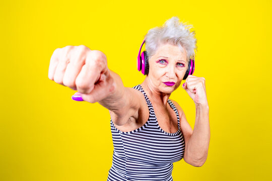 Elderly determinated woman practicing boxing on yellow background learning how to defend herself
