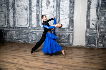 young man dancing with a girl in a blue ballroom dress in a gray dance hall