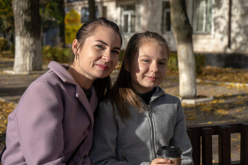 mother and daughter walking and drinking warm beverages outdoors. Coffee to go in a cups. autumn street photo